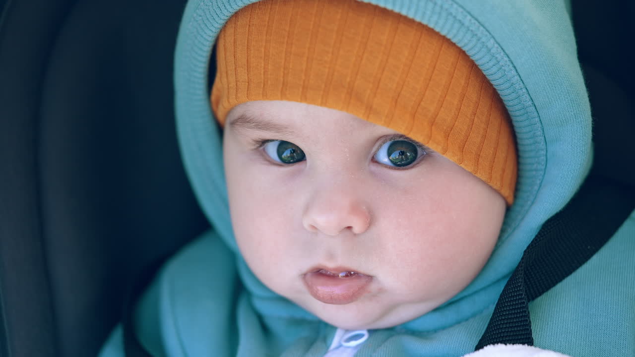Baby in warm clothes at walk. Beautiful peaceful child in cap looking calmly into camera. Close up portrait.