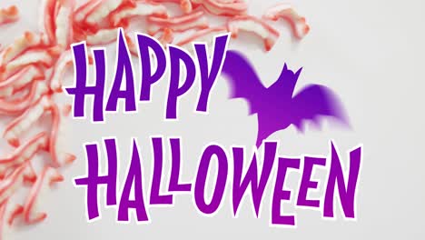 Happy-halloween-text-banner-with-bat-icon-against-halloween-candies-on-grey-surface