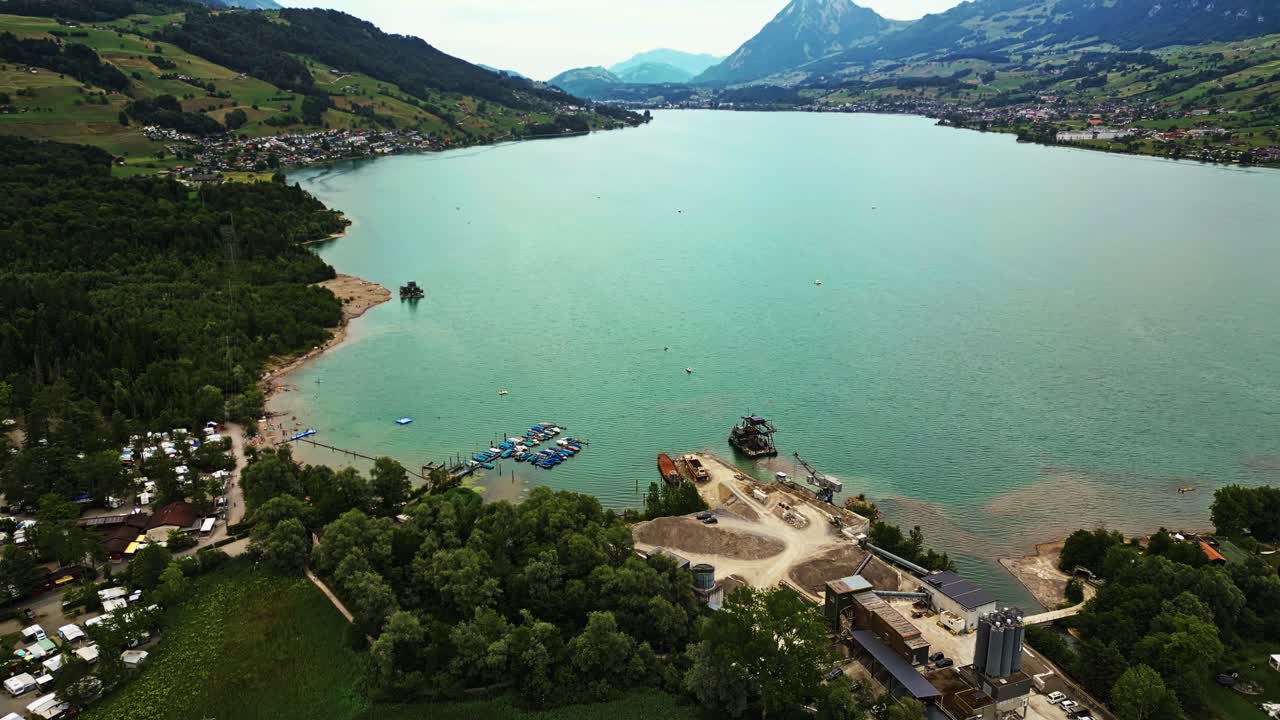 vista aérea de un lago prístino, con un muelle y barcos, en el borde de un pueblo, rodeado de montañas
