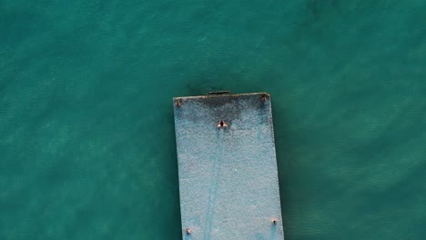 drone shot directly above of man on pier looking at clear blue sea