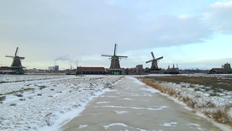 Flying-low-above-frozen-creek-towards-famous-Windmills-of-Zaanse-Schans-in-winter