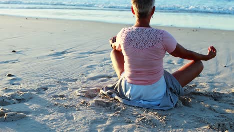 senior woman doing yoga on the beach