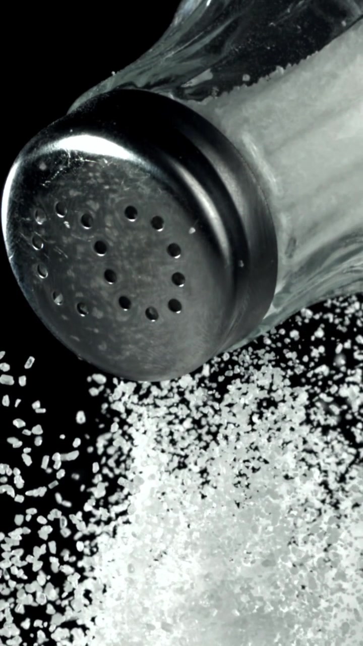 Primer plano de sal blanca vertiéndose de un salero sobre fondo negro