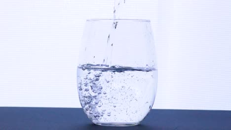 pouring fresh clean water splashing drops into a glass isolated on bright background