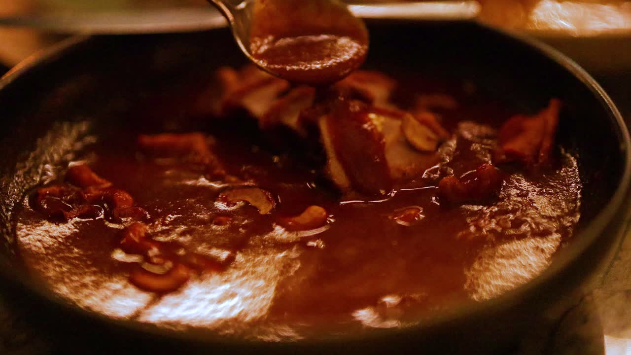 Close-up of a curry being stirred in a pan, showcasing rich colors and textures under warm lighting
