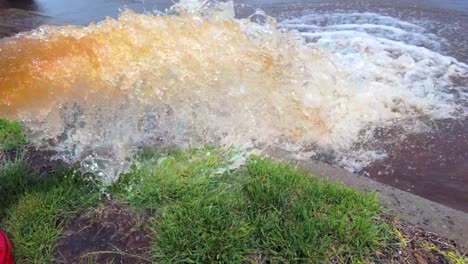 Eine-Aufnahme-Aus-Niedriger-Perspektive-Eines-Roten-Hydranten,-Der-An-Einem-Sonnigen-Tag-Rostiges-Wasser-Auf-Die-Straße-Sprüht