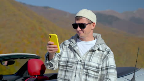 hombre usando teléfono cerca de descapotable en las montañas de otoño