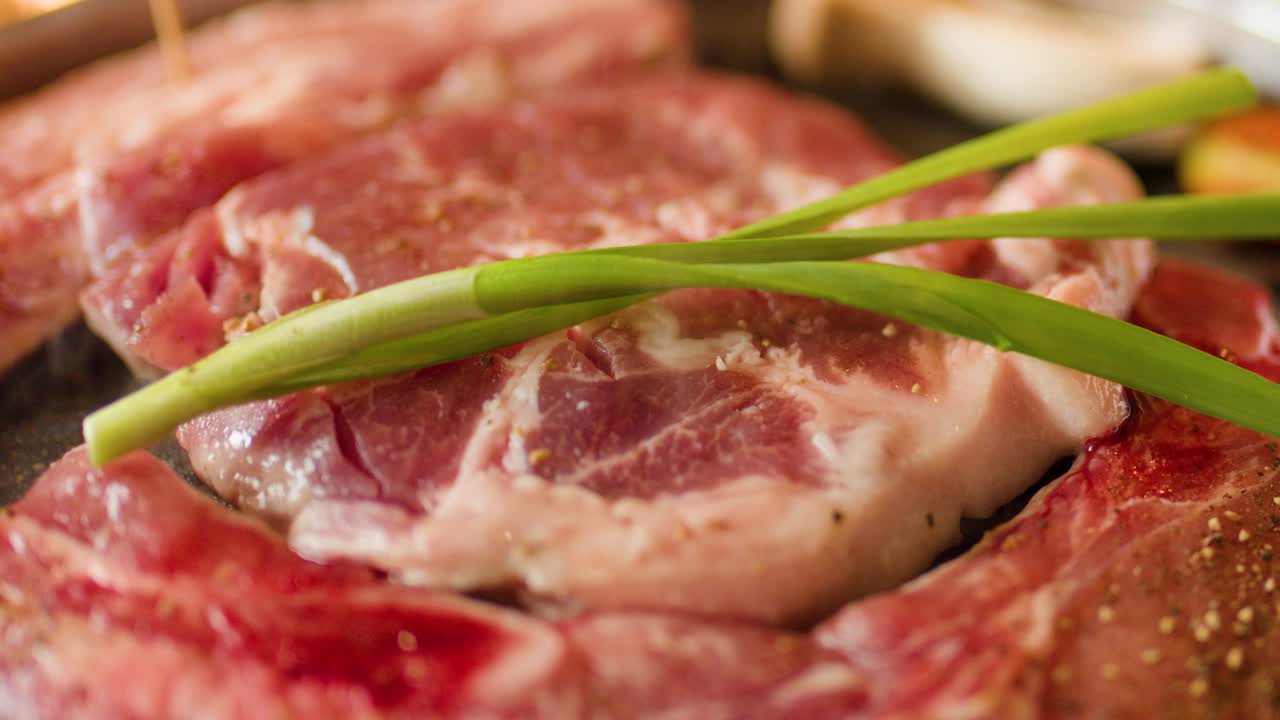 Raw beef and green onion grilling on hot pan, warm lighting, visible steam rising