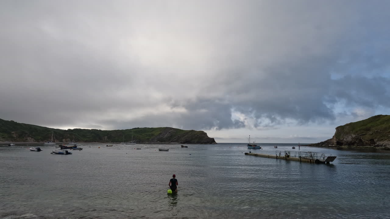 영국 도르 ⁇  의  ⁇ 워스 코브 에서 차가운 물 에 수영 하기 위해 바다 에 들어가는 여자