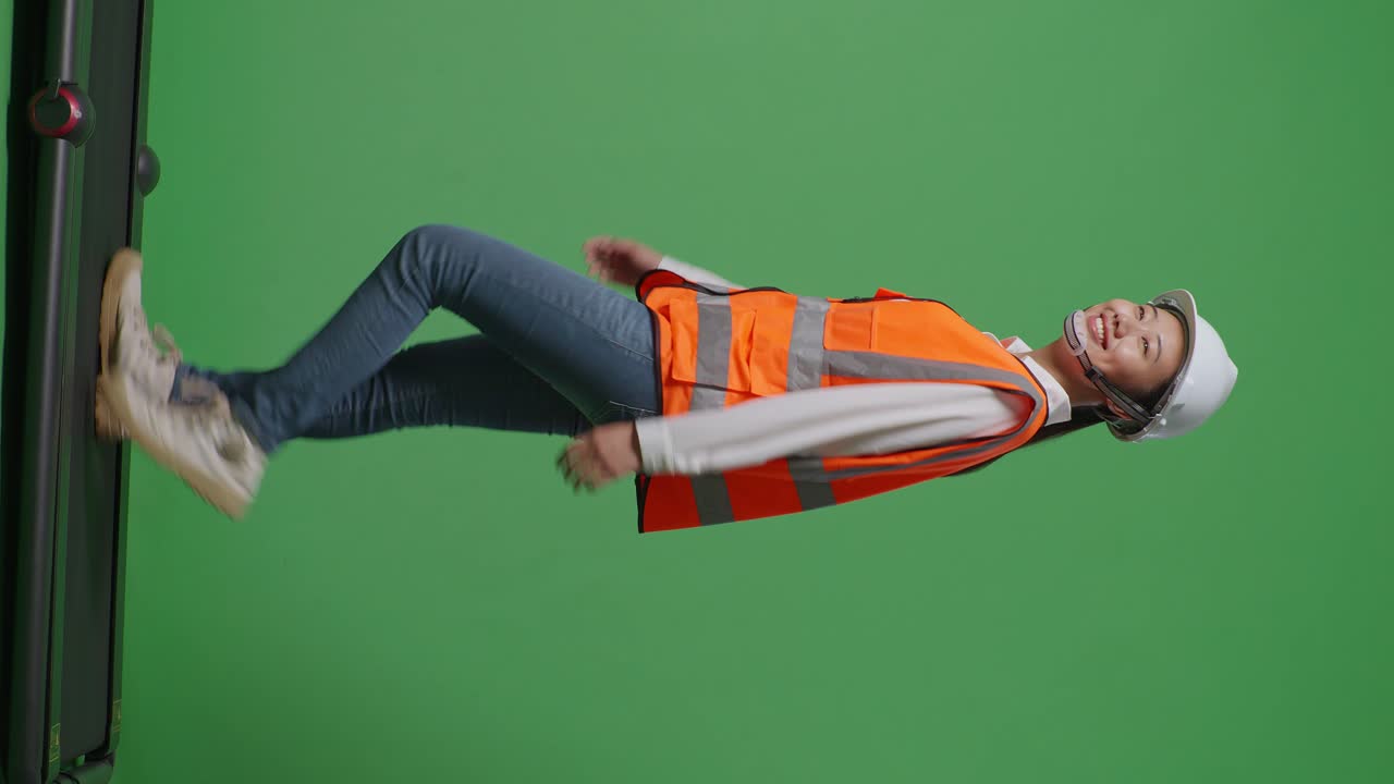 vista lateral de cuerpo completo ingeniera femenina asiática con casco de seguridad mirando a su alrededor mientras camina en el estudio de fondo de pantalla verde