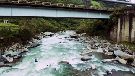 Zwei-Kajakfahrer-Rennen-Den-Fluss-Hinunter-Und-Passieren-Eine-Brücke-In-Den-Tiefen-Wald