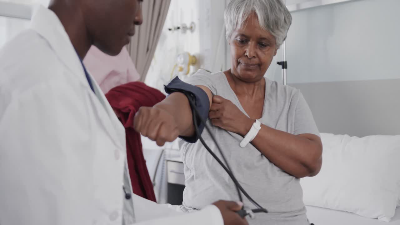 Diverse female doctor taking blood pressure of happy senior female patient in hospital, slow motion