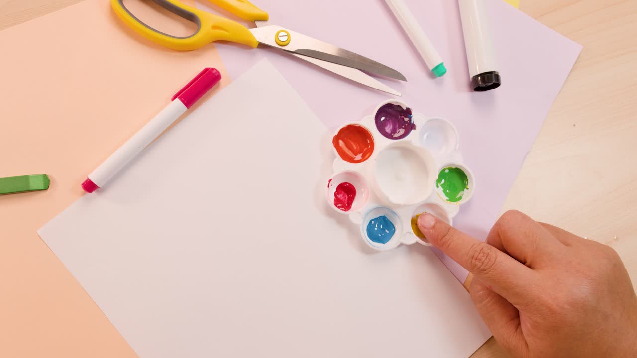 Person dips finger in yellow paint palette, preparing for finger painting on white paper