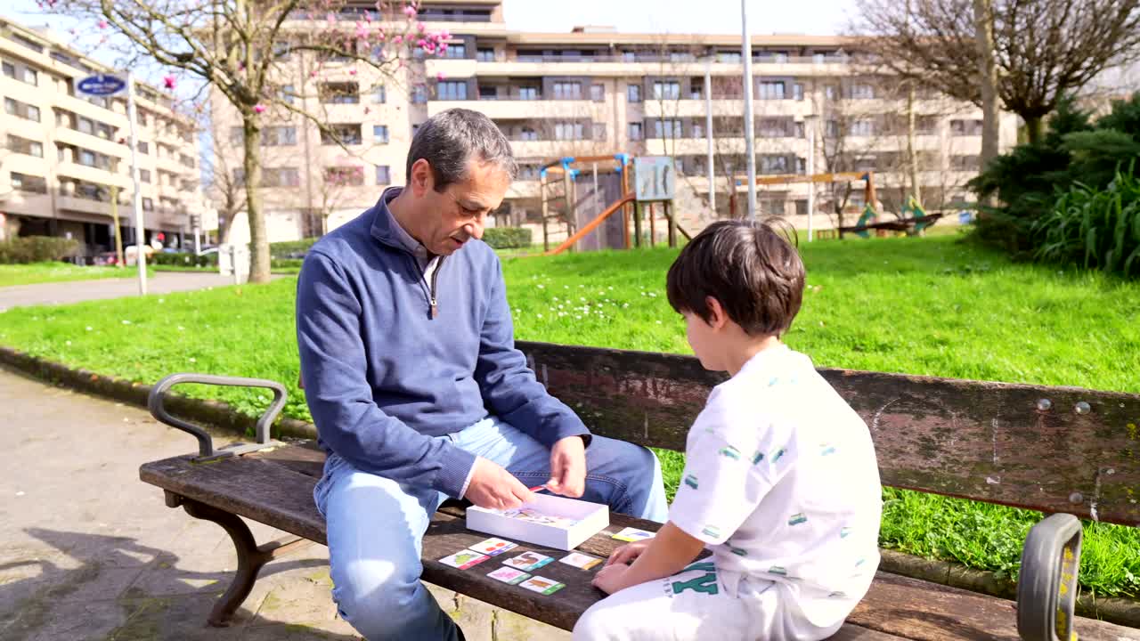 A man and child playing cards on a bench in a park