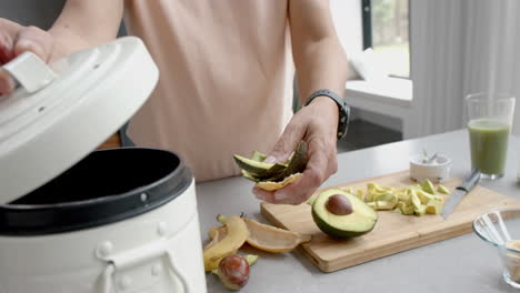 midsection of senior biracial man preparing smoothie, composting bio waste in kitchen, slow motion