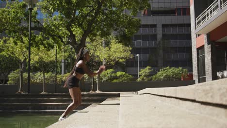 mujer afroamericana con auriculares inalámbricos haciendo ejercicio al aire libre saltando escaleras en la ciudad