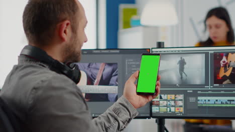 Editor-De-Vídeo-Hablando-Por-Videollamada-Sosteniendo-Un-Teléfono-Inteligente-Con-Pantalla-Verde