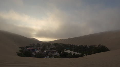 timelapse over huacachina peru south america in the morning sunrise on a cloudy grey day with the oasis between the dunes while the sun is coming up and reflection in the water