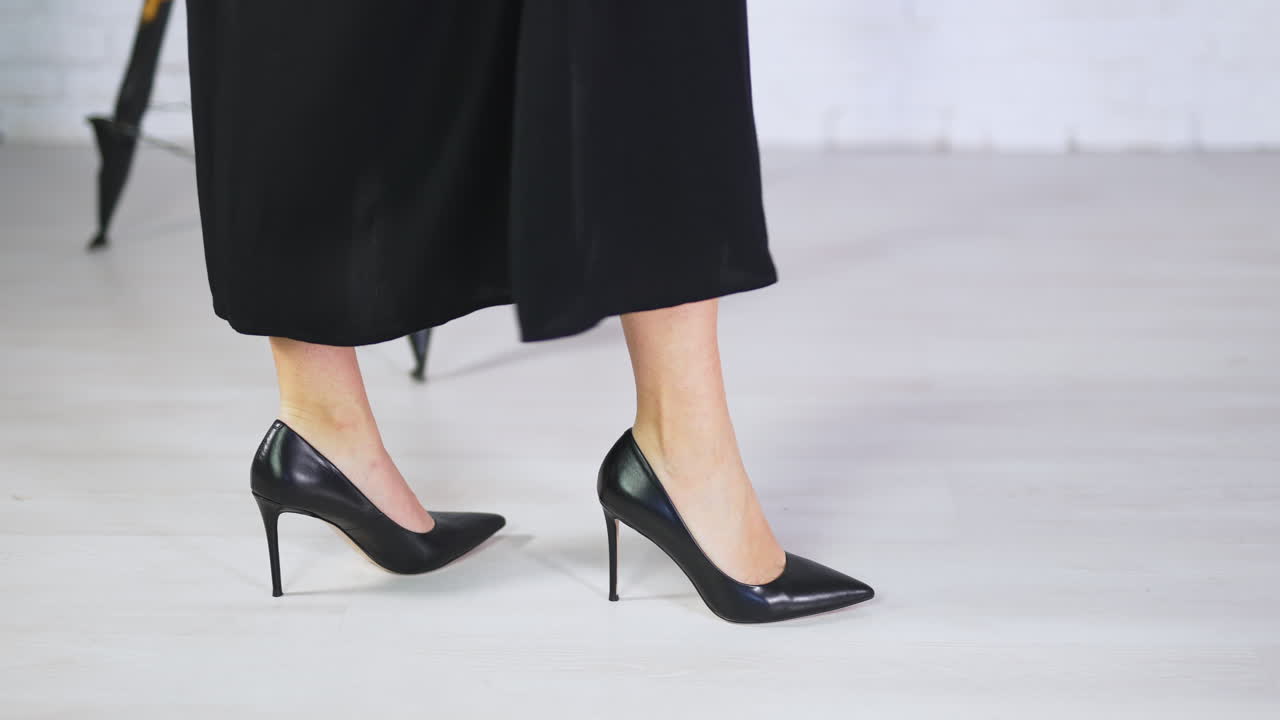 Model in long skirt demonstrates new shoes on very high heels. Showing footwear on a white backdrop. Close up.