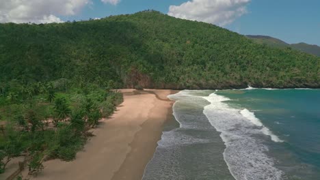 Aerial-backwards-shot-of-beautiful-sandy-beach,-ocean-waves-and-green-mountains---In-background-SAN-JUAN-RIVER-MOUTH,-SAMANA-VALLEY,-DOMINICAN-REPUBLIC