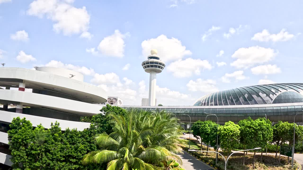 Camera moves toward airport parking, glass dome, and control tower in bright daylight