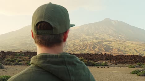 man wearing green hoodie and baseball cap looks afar towards the mountain, handheld closeup