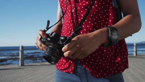 african american woman standing and holding camera on promenade by the sea