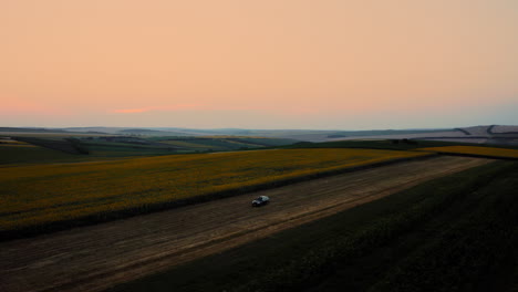 Car-Off-Road-in-Vast-Field-Terrain-at-Sunset-With-Golden-Sky,-Aerial-Drone-Orbital-View