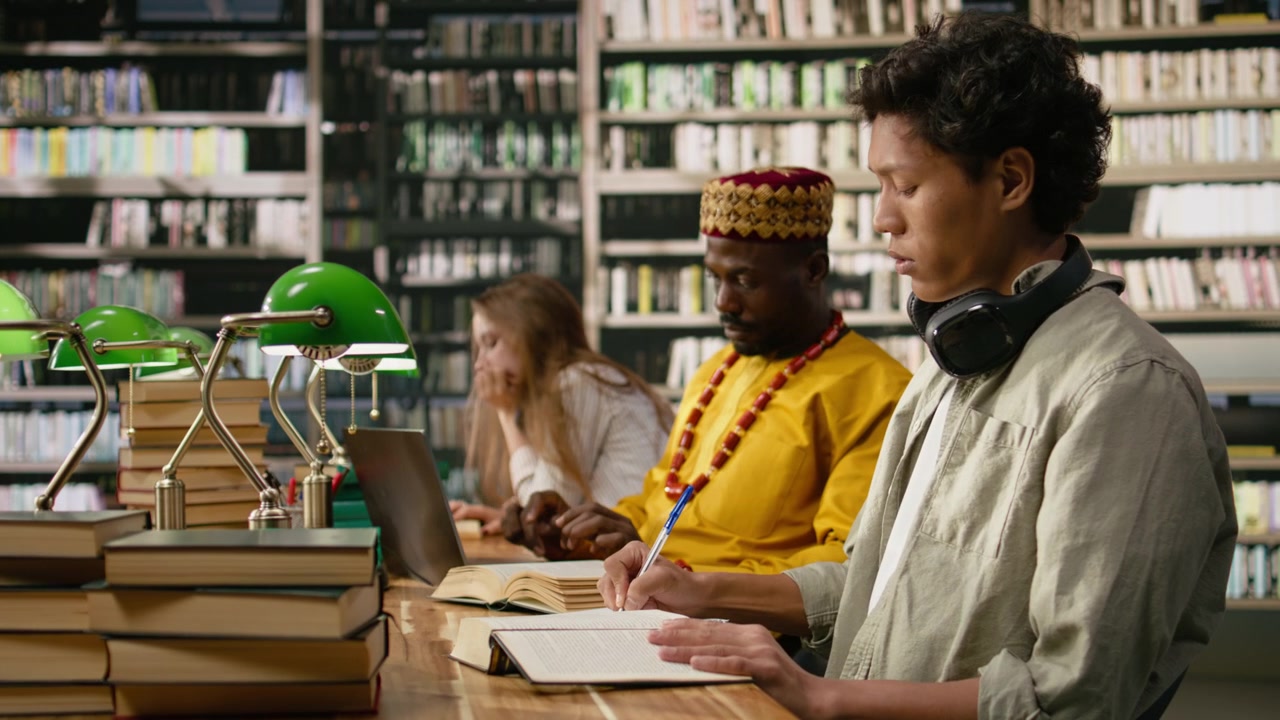 Student reading open book at library desk near chatbot on computer screen
