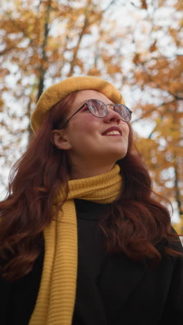 dama elegante en boina amarilla gira hoja de otoño en la mano mientras pasea por el parque vibrante lleno de follaje dorado, tomando el sol cálido y disfrutando de la naturaleza pacífica con encanto gracioso