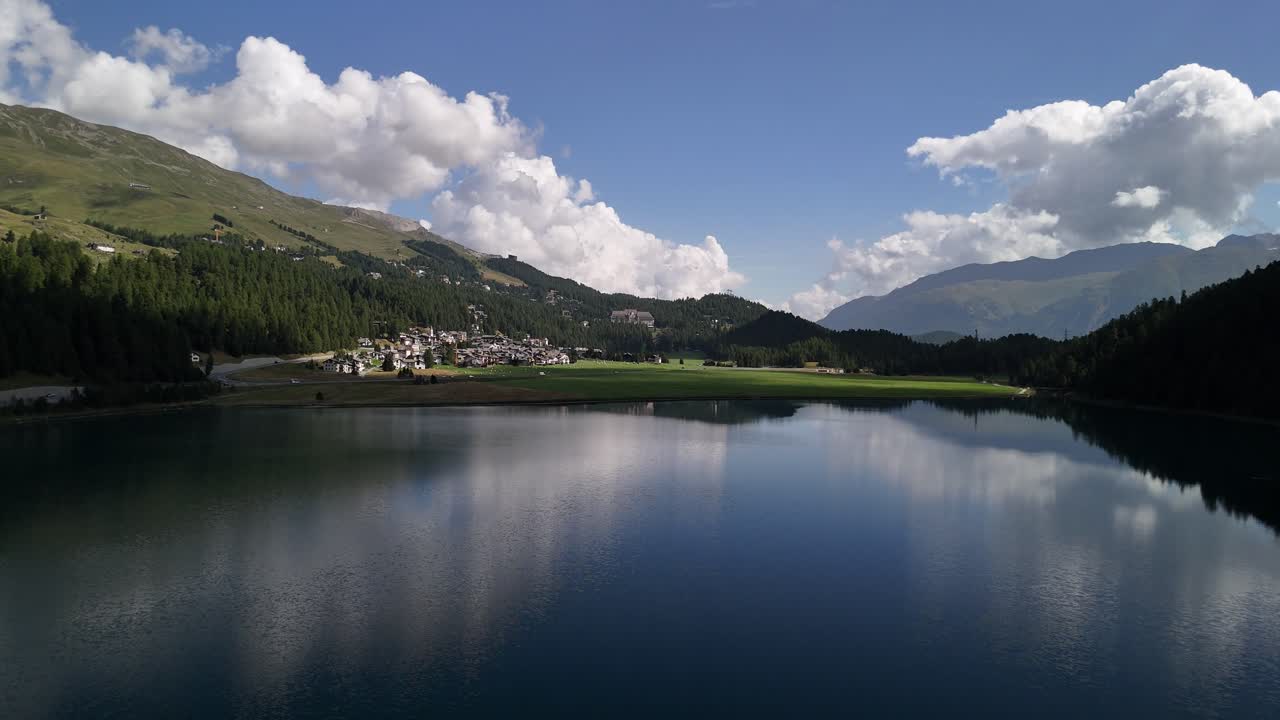 Aerial view of the calm lake surface of Silvaplanersee in Graubünden, Switzerland, with serene waters reflecting a quiet residential area along the shoreline.