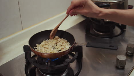 woman hand stirring almond nuts fried in a metal pan, on a gas cooking pan