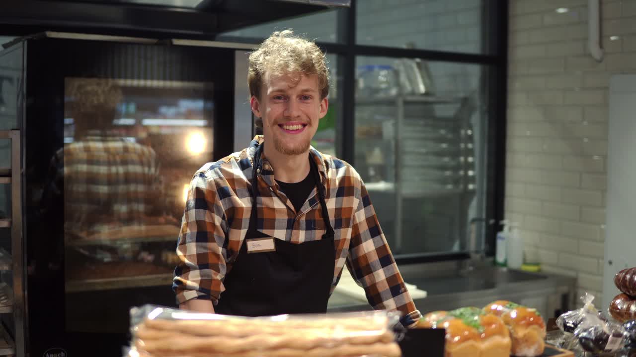 Portrait of the handsome man baker in plaid shirt and apron smiling to the camera and posing in the bakery shop. Close up. Indoor