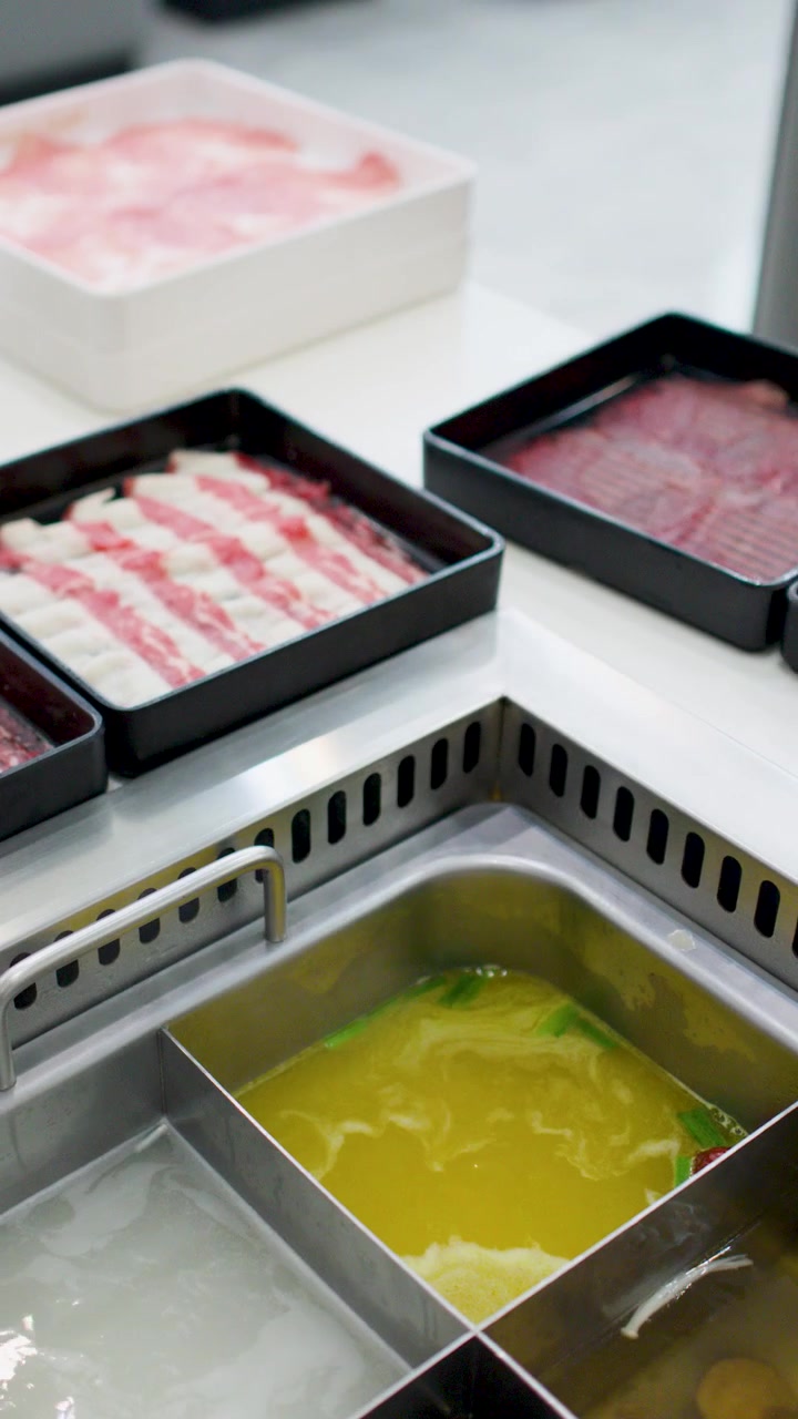 Des mains disposent des plateaux de bœuf et de porc crus finement tranchés sur une table pour le shabu-shabu.