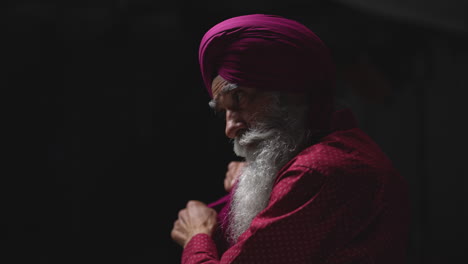 Primer-Plano,-Toma-De-Estudio-Con-Iluminación-Tenue-De-Un-Hombre-Sikh-Mayor-Con-Barba-Atando-Una-Tela-Para-Un-Turbante-Contra-Un-Fondo-Oscuro,-Filmado-En-Tiempo-Real