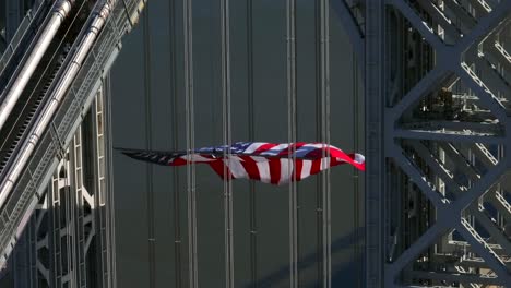 Una-Vista-Aérea-De-La-Torre-En-El-Lado-De-Nueva-Jersey-Del-Puente-George-Washington-Con-Una-Bandera-Estadounidense-Gigante-Ondeando-En-Un-Día-Soleado