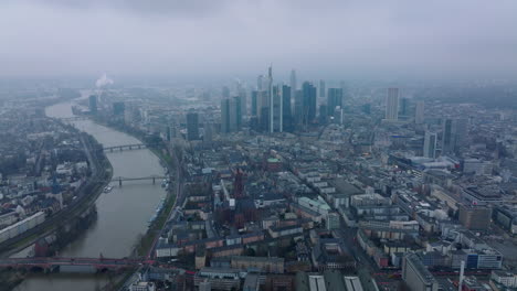 Fly-above-metropolis.-Group-of-downtown-skyscrapers-towering-above-town-development.-Bridge-spanning-wide-river.-Frankfurt-am-Main,-Germany