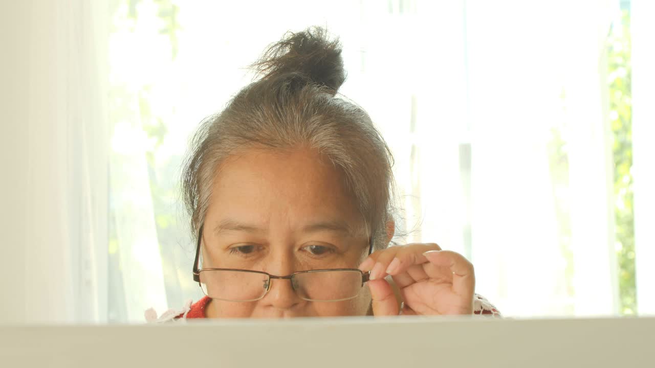 mujeres ancianas asiáticas con gafas trabajan en casa en la computadora portátil