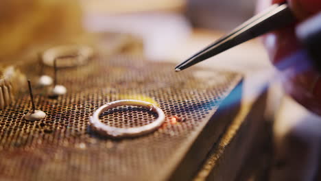 close up of female jeweller working on ring in studio using blowtorch