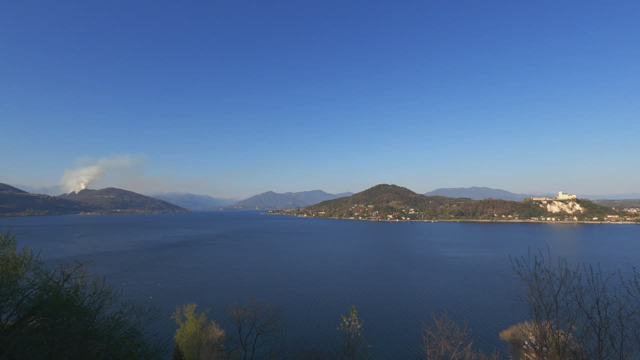 Panoramic view over Maggiore lake and smoke from mountain due to burning fire close to Nebbiuno in Piedmont, Italy