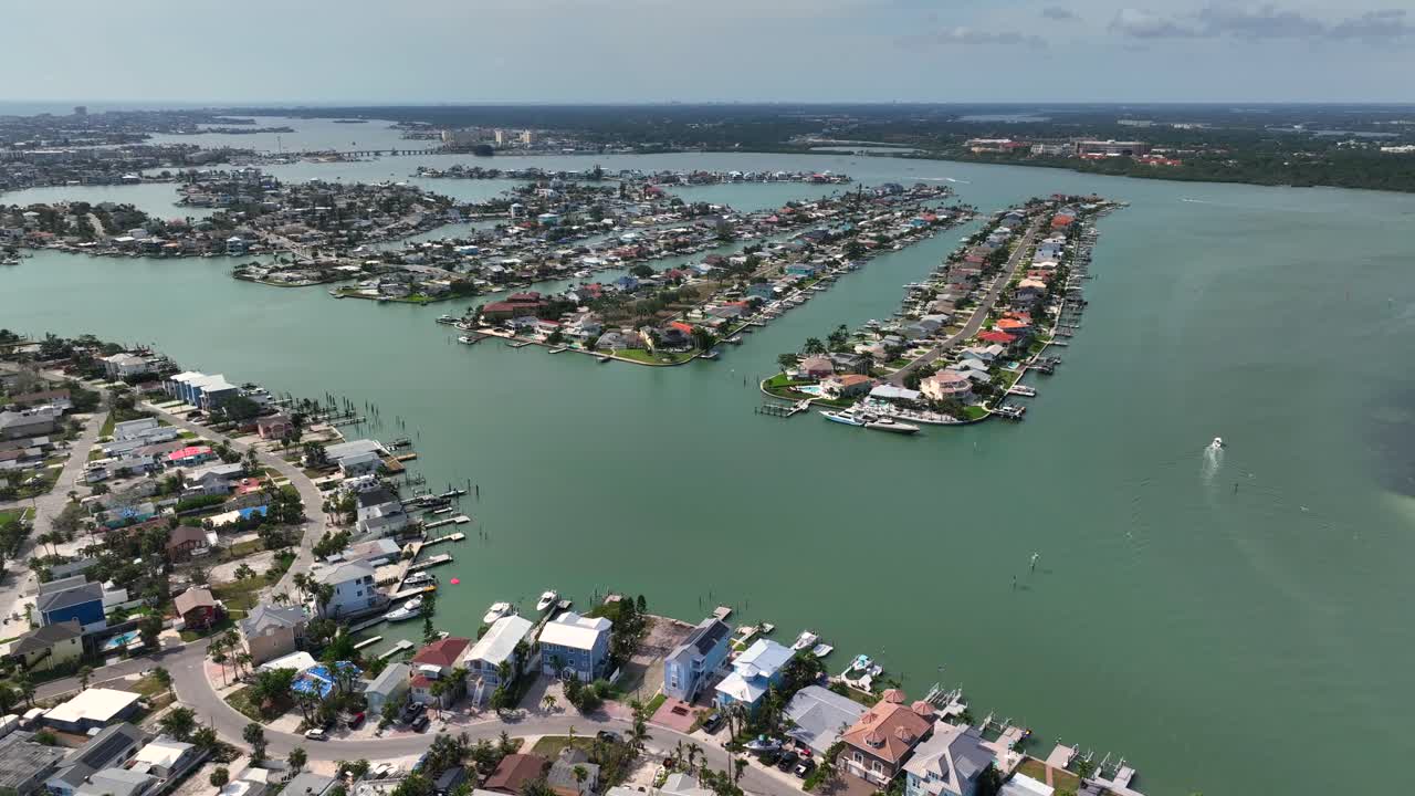Madeira Beach Town in Florida with luxury houses in islands at sunny day. Aerial wide shot. Parking boats on pier. Crystal island with houses and homes in United States. Palm trees along Roads.