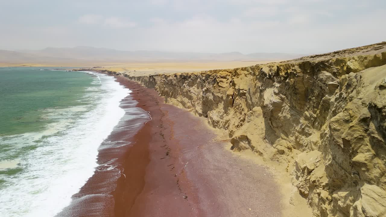 Aerial flyby along the Playa Roja Red Sand Beach with dramatic coastal cliffs and turquoise surf in Paracas National Reserve Peru