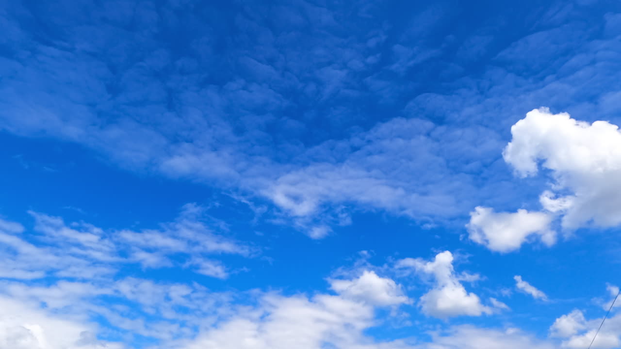 Stratocumulus clouds float in the atmosphere. Low angle view on the soft clouds moving in the blue sky. Timelapse.
