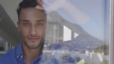 retrato de un hombre biracial feliz mirando por la ventana y sonriendo, en cámara lenta