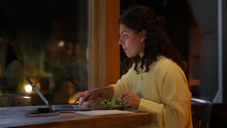 mujer trabajando desde casa por la noche mientras come ensalada