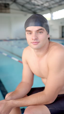 vertical video: swimmer in swim cap sitting by pool, preparing for training session