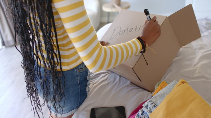 Writing on donation box, woman preparing clothes for charity at home