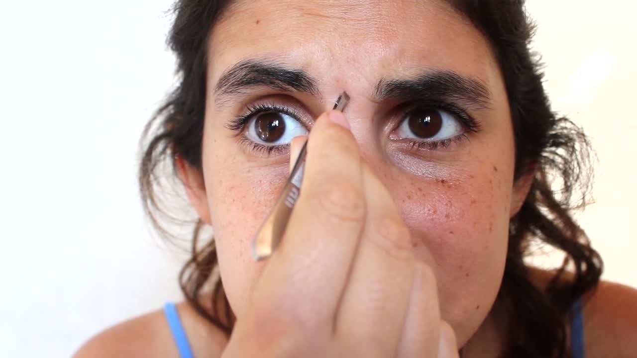 mujer joven depilándose las cejas con pinzas aisladas en blanco