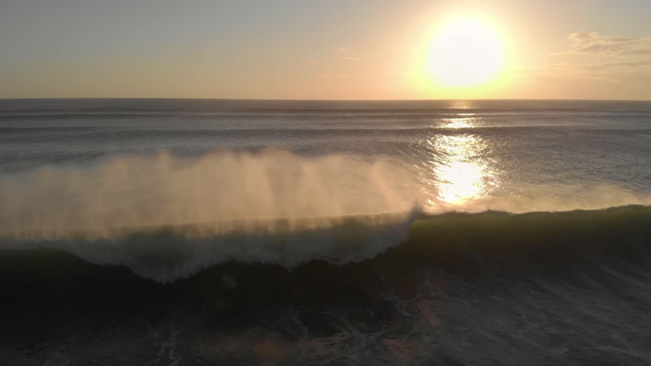 volando hacia atrás sobre un océano al atardecer, siguiendo una gran ola rodante