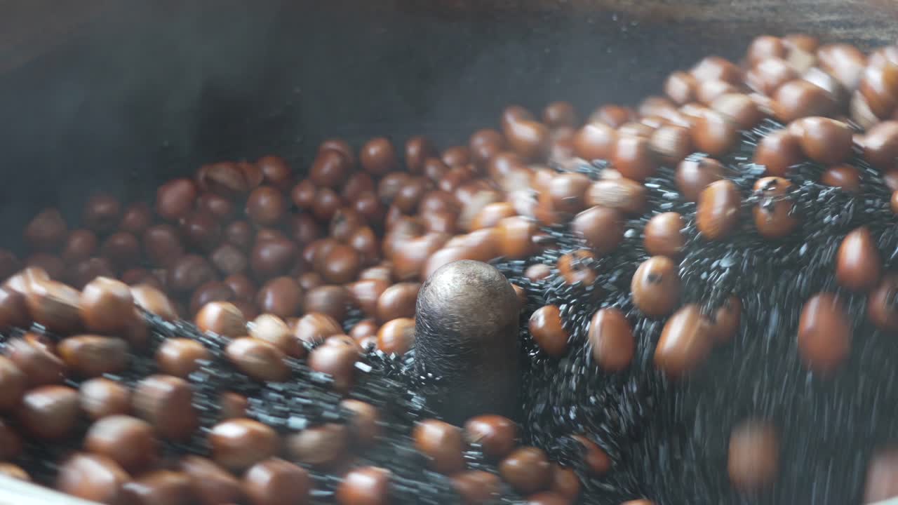 Close-up of a traditional street food vendor on Yaowarat Road, Bangkok, showing a motorized tumbler roasting Chinese chestnuts with black beans, a signature delicacy of Chinatown's culinary scene